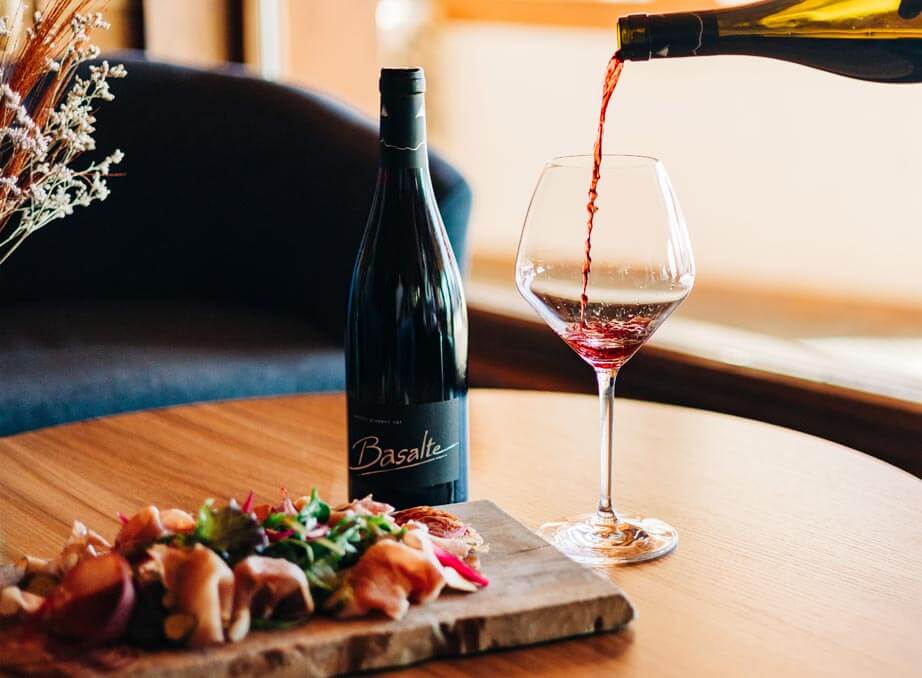 Verre de vin rouge en train d'être servie d'un Gamay vieilles vignes, AOP Côte d'Auvergne, accompagné d'une planche de charcuterie gourmande