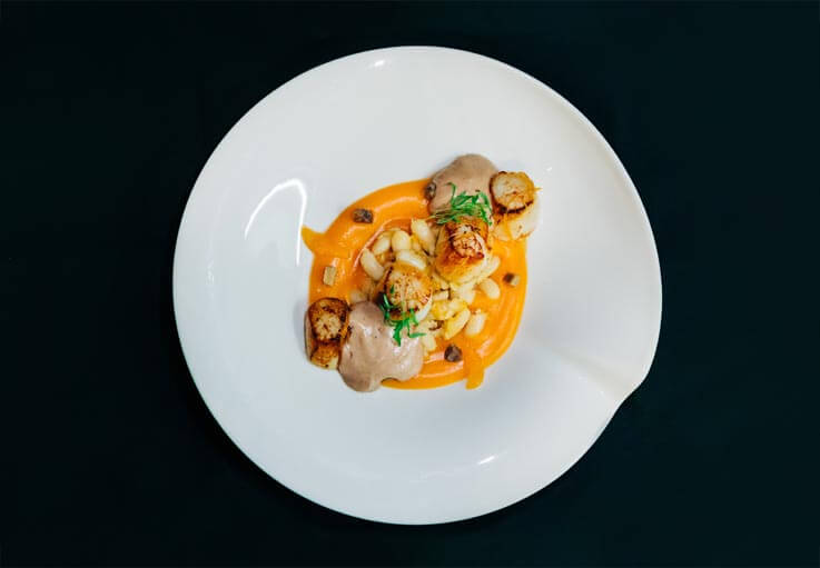 Plat, vue de dessus, de coquilles Saint-Jacques fraichement pêchées dans la Baie d'Erquy, en bretagne, accompagnées d'un délicat ensemble de potimarron, de mandarine corse et de chataigne